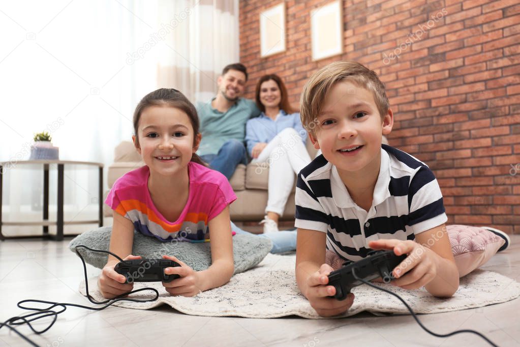 Cute children playing video games while parents resting on sofa at home