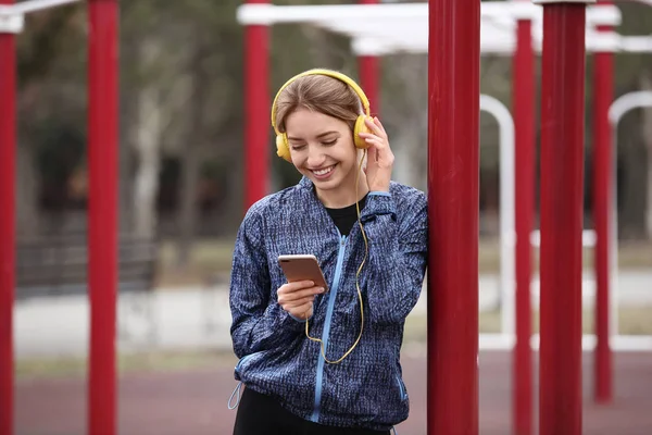 Young woman with headphones listening to music on sports ground