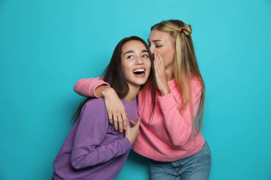 Genç kadın arkadaşı renk arka planı komik bir şey fısıldayan süre gülüyor