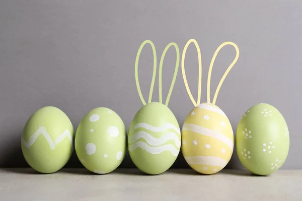 一套彩绘的鸡蛋与复活节兔子耳朵在桌子对灰色背景 — 图库照片