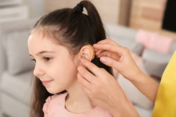 年轻女子在室内将助听器放在女儿的耳朵里 — 图库照片