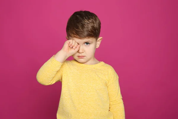 Little boy rubbing eye on color background. Annoying itch