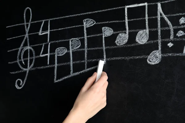 Woman writing music notes with chalk on blackboard, closeup