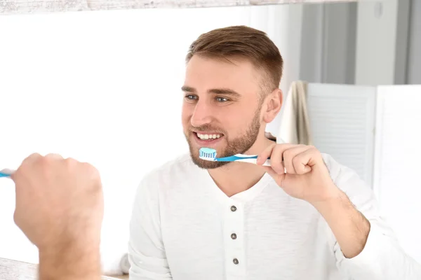 Young man cleaning teeth against mirror in bathroom