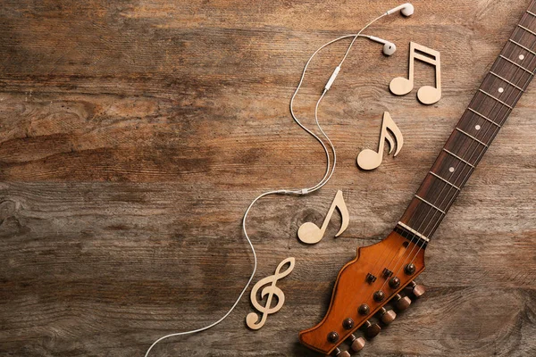 Guitar neck, earphones and music notes on wooden background, flat lay. Space for text