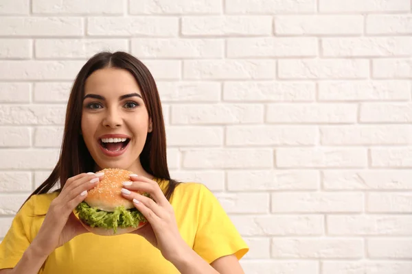 レンガの壁の近くのおいしいハンバーガーを食べる若い女性 テキストのためのスペース — ストック写真