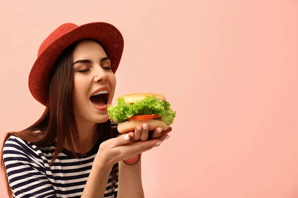 背景色でおいしいハンバーガーを食べる若い女性 テキストのためのスペース — ストック写真