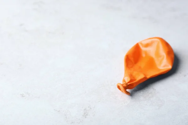 Orange deflated balloon on grey background, space for text