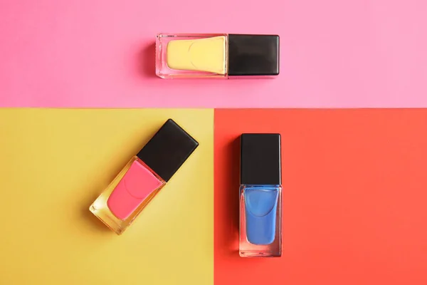 Bottles of nail polish on color background, top view