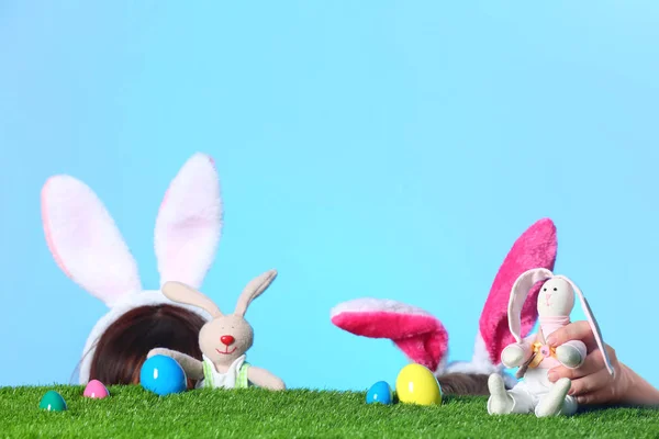 小女孩戴着兔子耳朵头巾 在绿色背景的绿草表面玩玩具复活节兔子 — 图库照片
