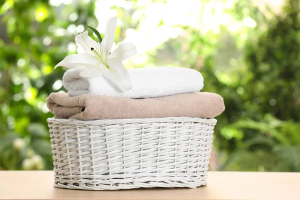 Basket with soft bath towels and flower on table against blurred background