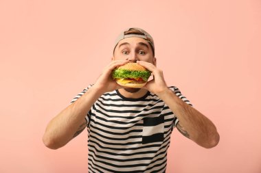 Genç adam renk arka plan üzerinde lezzetli hamburger yeme