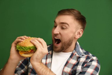 Genç adam renk arka plan üzerinde lezzetli hamburger yeme