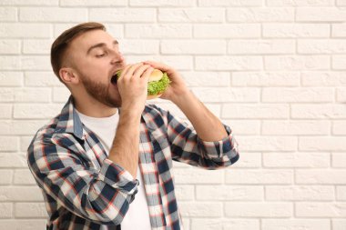 Genç adam tuğla duvar yakınındaki lezzetli hamburger yeme. Metin için yer