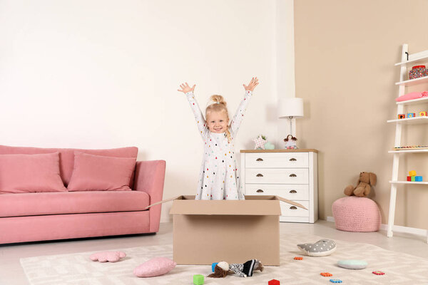 Cute little girl playing with cardboard box at home