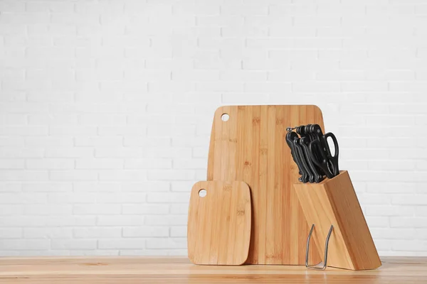 Holder with knives and clean boards on table against white brick wall. Space for text