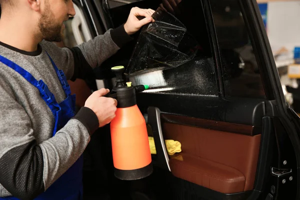 Skilled worker tinting car window in shop