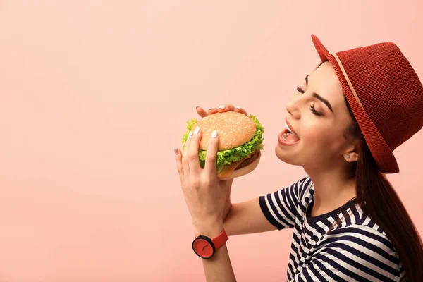 背景色でおいしいハンバーガーを食べる若い女性 テキストのためのスペース — ストック写真