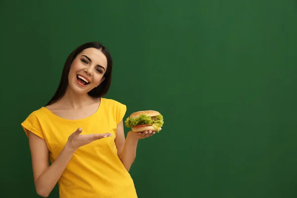 背景色でおいしいハンバーガーを持つ若い女性 テキストのためのスペース — ストック写真