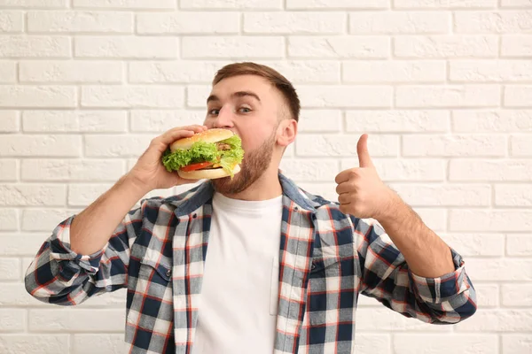 Genç adam tuğla duvara lezzetli hamburger yeme