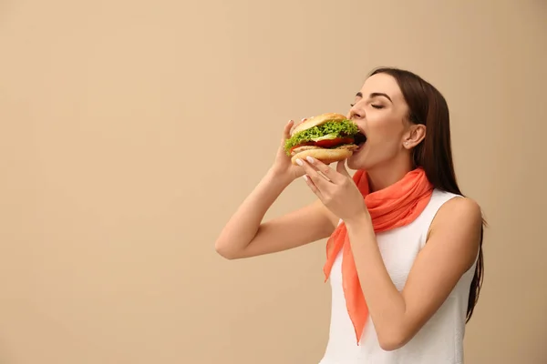 年轻女子在颜色背景上吃美味的汉堡 文本的空间 — 图库照片
