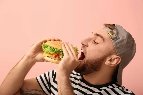 Young Man Eating Tasty Burger Color Background — Stock Photo, Image