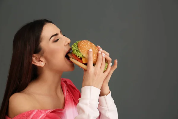 Young Woman Eating Tasty Burger Grey Background Space Text — Stock Photo, Image