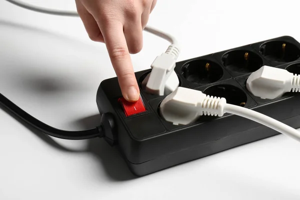 Woman pressing power button of extension cord on white background, closeup. Electrician's equipment