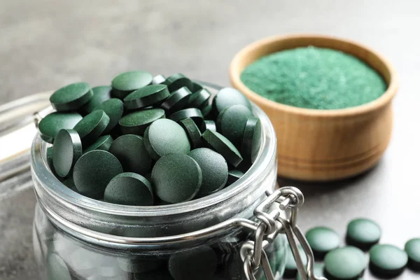 Glazen Pot Met Groene Spirulina Pillen Grijze Tafel Close — Stockfoto