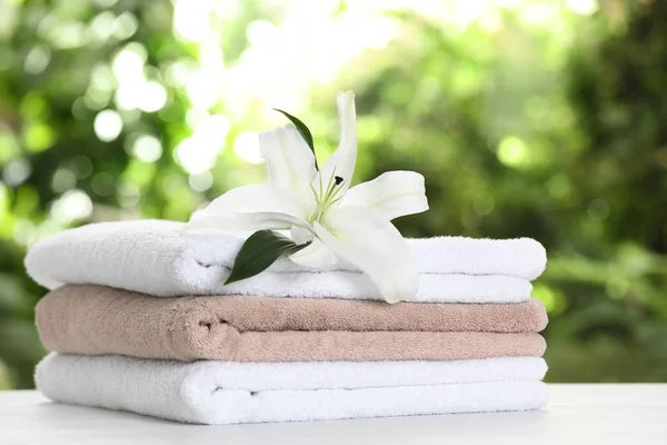 Stack of clean soft towels and flower on table against blurred background