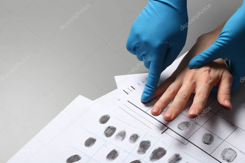 Investigator taking fingerprints of suspect on grey table, closeup. Space for text
