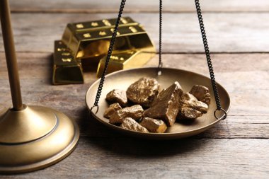 Scale pan with gold lumps on wooden table, closeup clipart