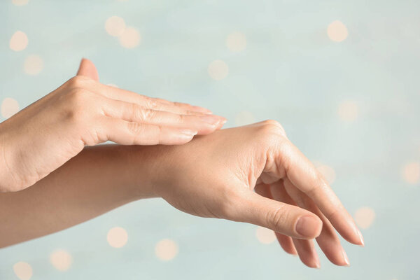 Woman applying hand cream on blurred background, closeup