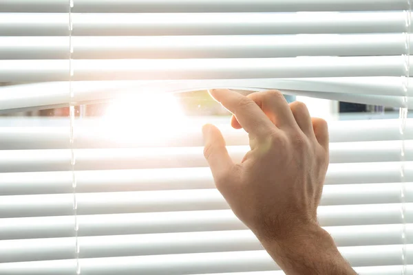 Young man opening window blinds, closeup. Space for text