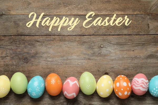 Flache Liegekomposition aus bunt bemalten Eiern und Text frohe Ostern auf Holzgrund — Stockfoto