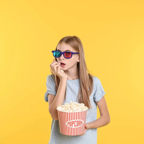 Emotional teenage girl with 3D glasses and popcorn during cinema show on color background — Stock Photo, Image