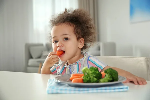 可爱的非洲裔美国女孩在客厅的桌子上吃蔬菜 — 图库照片