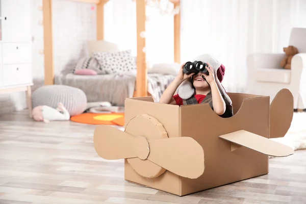 Lindo niño jugando con prismáticos y avión de cartón en el dormitorio — Foto de Stock