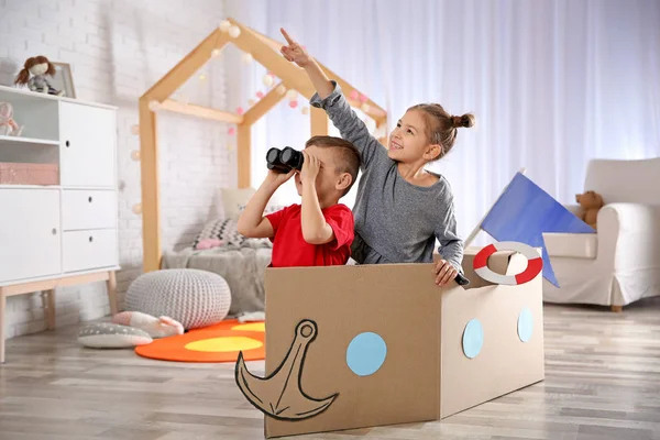 Lindos niños pequeños jugando con prismáticos y barco de cartón en el dormitorio — Foto de Stock