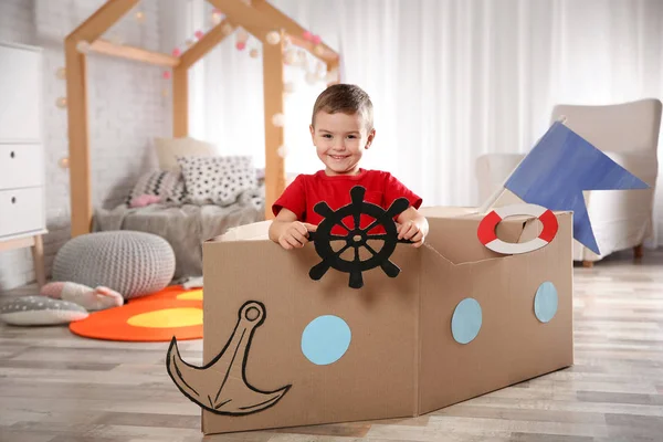 Anak kecil yang lucu bermain dengan perahu kardus di kamar tidur — Stok Foto