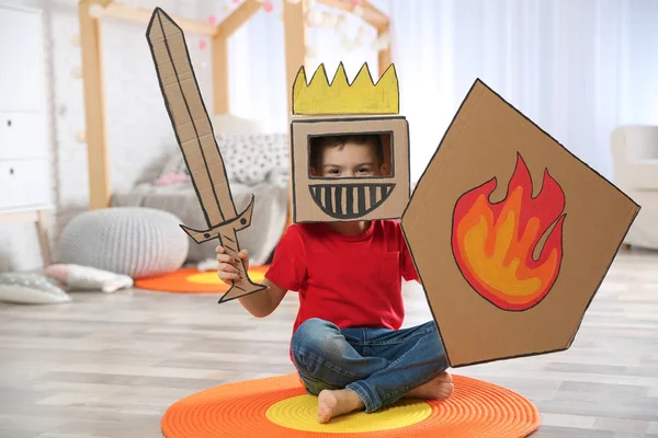 Lindo niño jugando con armadura de cartón en el dormitorio —  Fotos de Stock