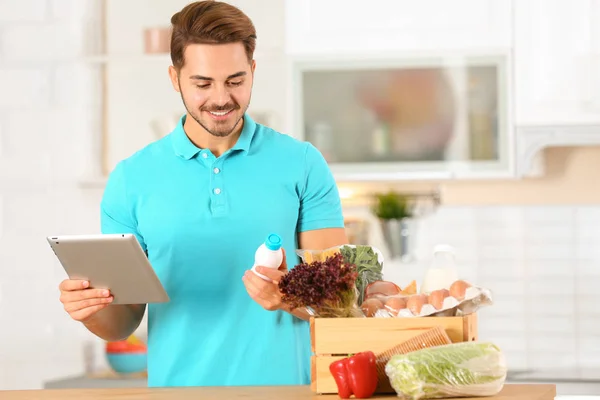 Joven con tablet PC y productos en cocina. Servicio de entrega de alimentos —  Fotos de Stock