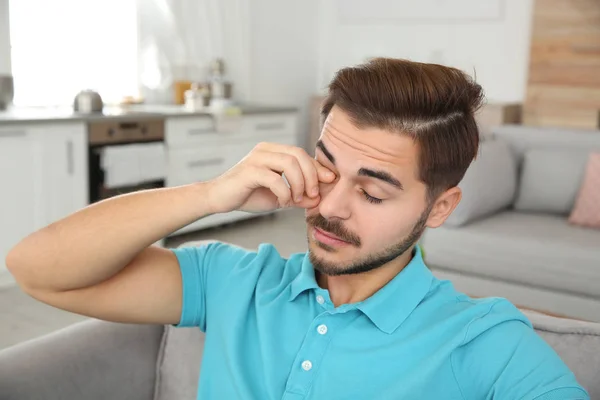 Young man rubbing eye at home. Annoying itch