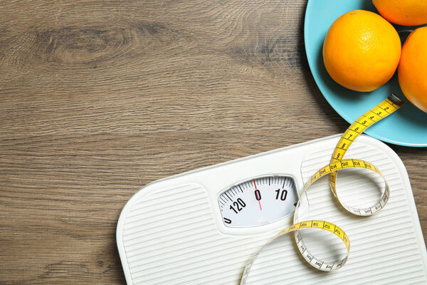 Scales, measuring tape, oranges and space for text on wooden background, top view. Weight loss