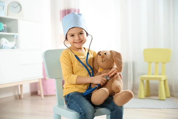 Lindo niño imaginándose a sí mismo como médico mientras juega con estetoscopio y conejito de juguete en casa —  Fotos de Stock