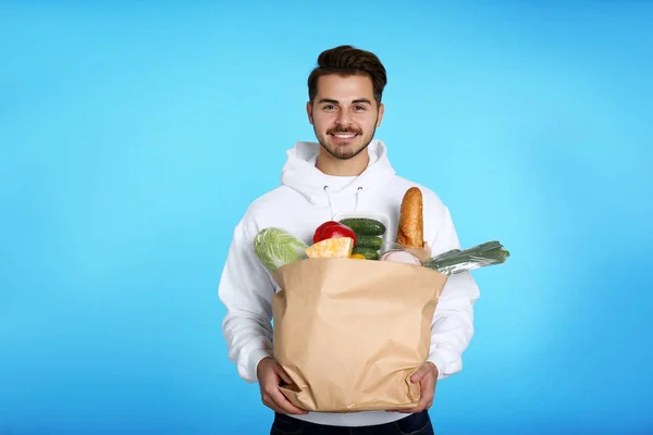 Junger Mann mit Papiertüte mit Produkten auf farbigem Hintergrund. Essenslieferdienst — Stockfoto