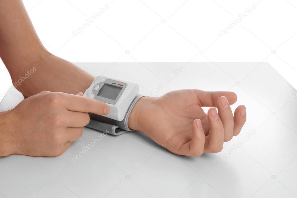 Man checking blood pressure with sphygmomanometer at table against white background, closeup. Cardiology concept