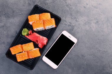Lezzetli suşi rulo ve smartphone ile metin gri tablo, en iyi görünüm için yer. Food teslim
