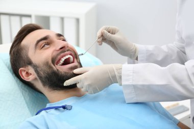 Dişçi genç adamın dişlerini hastanede ayna ile incelenmesi