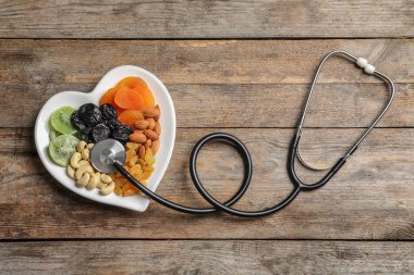 Plaka ile fındık ve kuru meyve stetoskop ahşap arka plan, üstten görünüm üzerinde yakınındaki kalp şeklinde